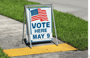 A sandwich board that reads "VOTE HERE MAY 9"