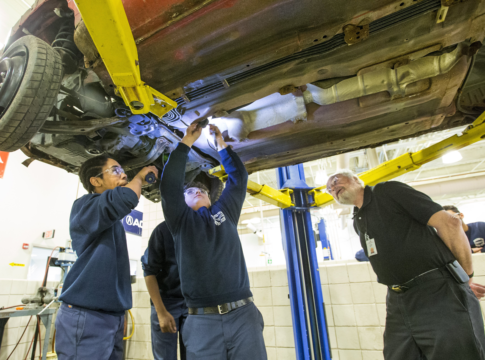 Worcester Technical High School teacher Louis Desy, right, watches as Zaire Peart, left, holds a flashlight for Kyle Dipilato, who is disassembling a car donated by a local salvage company.