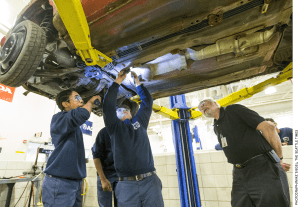 Worcester Technical High School teacher Louis Desy, right, watches as Zaire Peart, left, holds a flashlight for Kyle Dipilato, who is disassembling a car donated by a local salvage company.