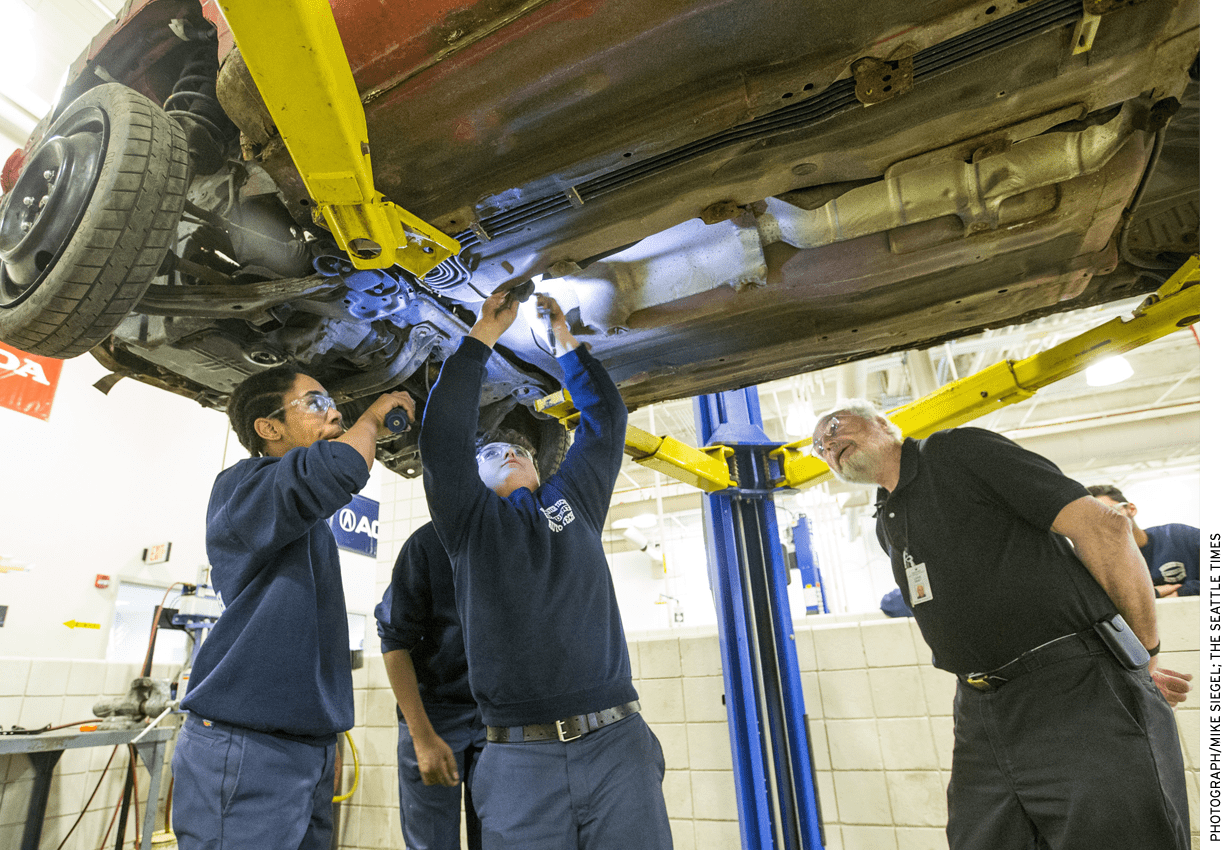 Worcester Technical High School teacher Louis Desy, right, watches as Zaire Peart, left, holds a flashlight for Kyle Dipilato, who is disassembling a car donated by a local salvage company.