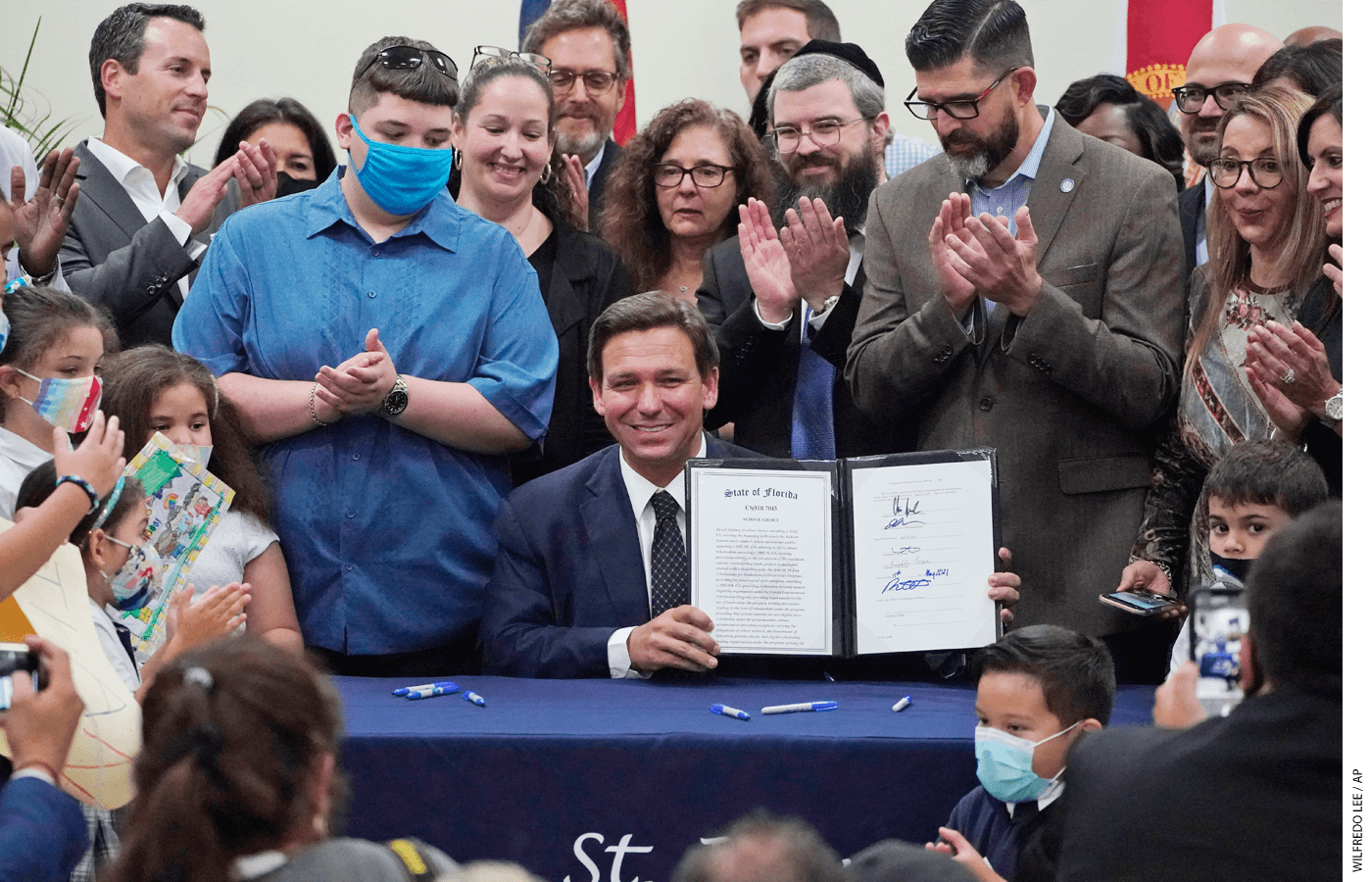 Florida Gov. Ron DeSantis, seated, celebrates after signing a bill that expands eligibility for state scholarships to fund private-school tuition.