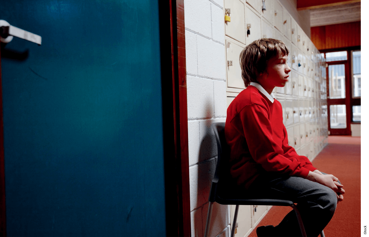 A student sits in the hallway next to a closed door.