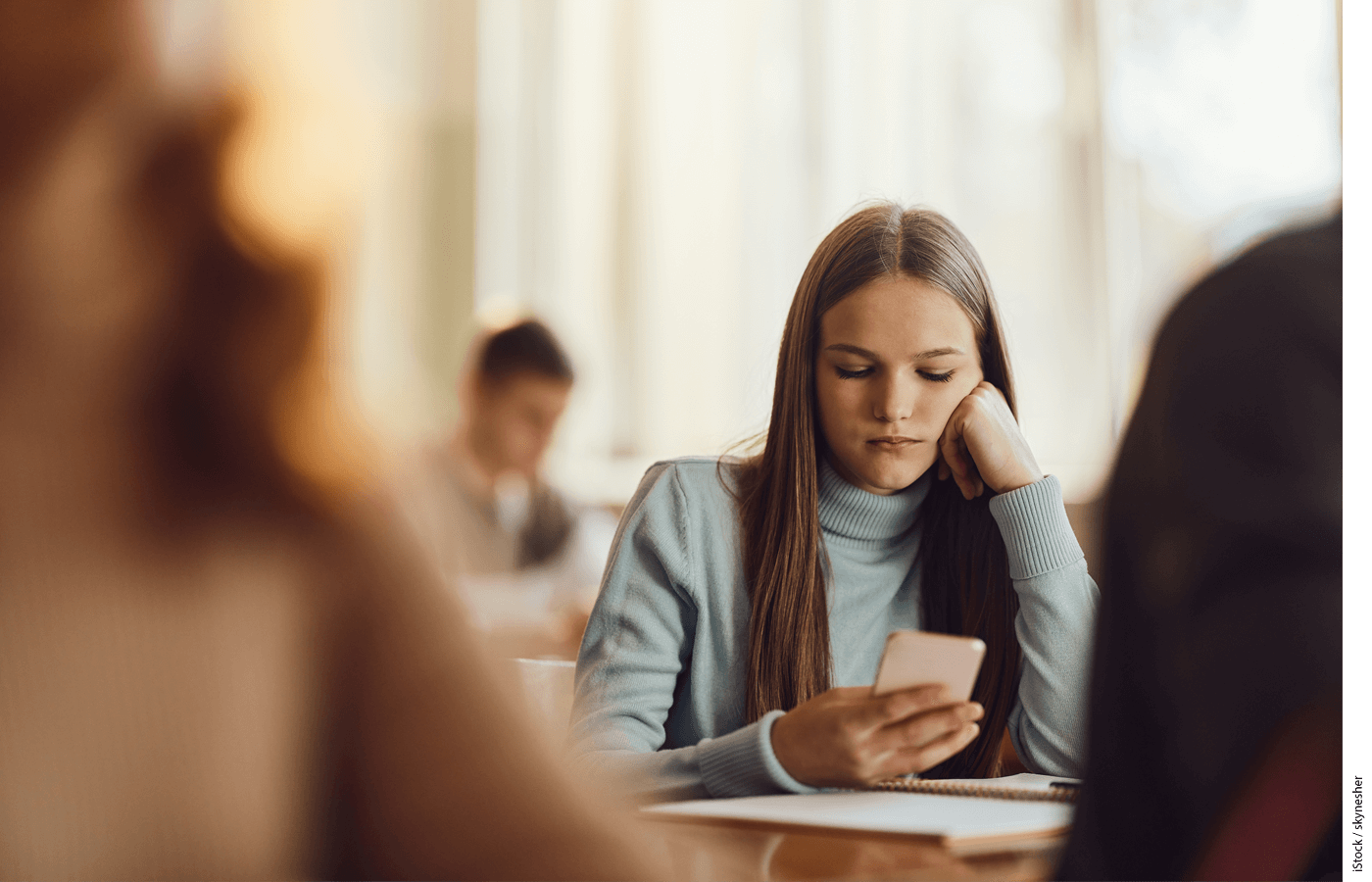 A bored female student using cell phone in class at school.