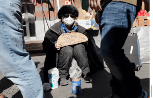 A homeless woman going by the name of Miss Bee seeks donations at an outdoor produce market in Boston, Saturday, March, 14, 2020.