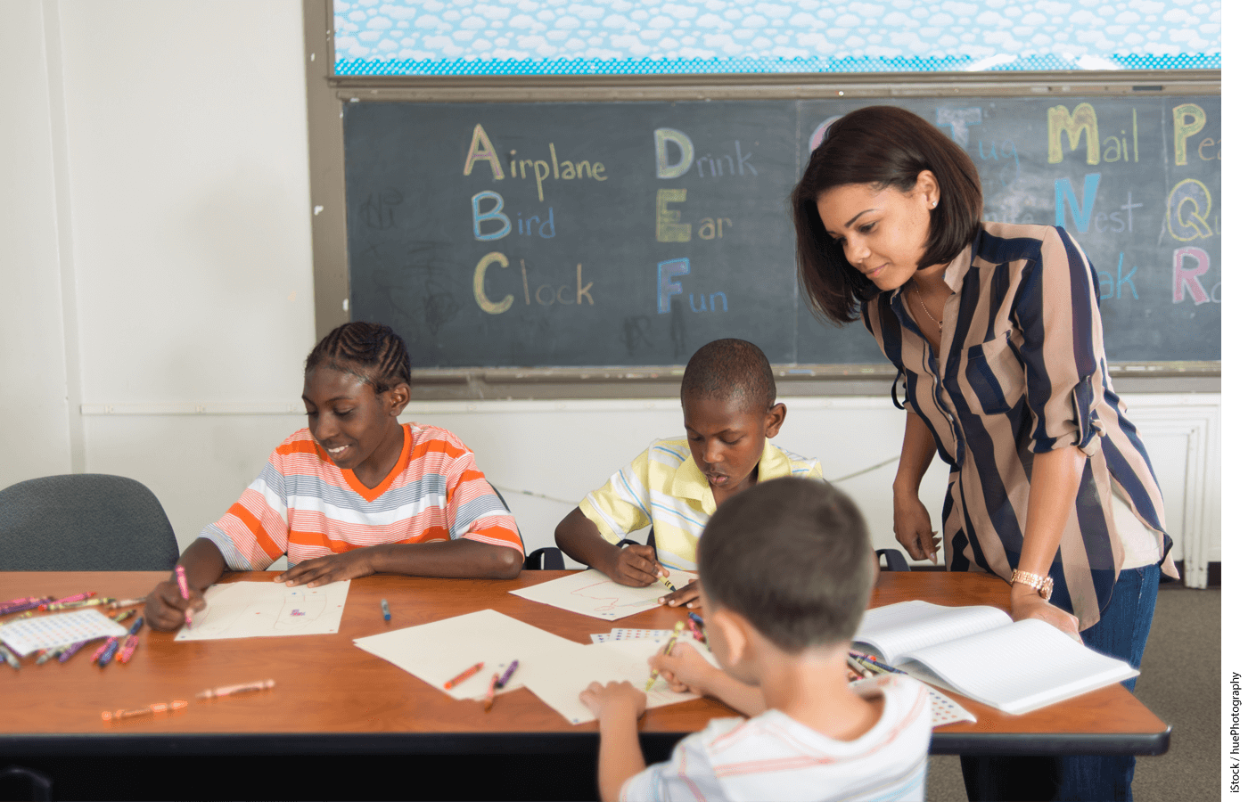 Multi-racial inner city school students in classroom working on an assignment as the teacher watches over them.