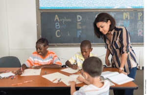 Multi-racial inner city school students in classroom working on an assignment as the teacher watches over them.